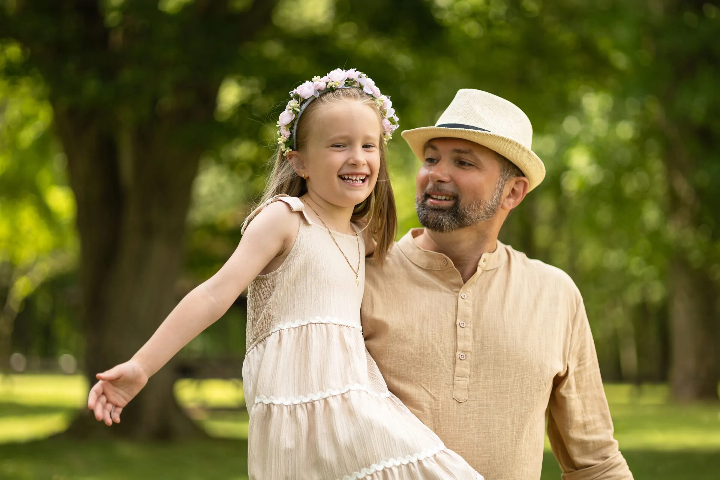 Laughing girl in a flower crown with her arms out next to her dad in a straw hat