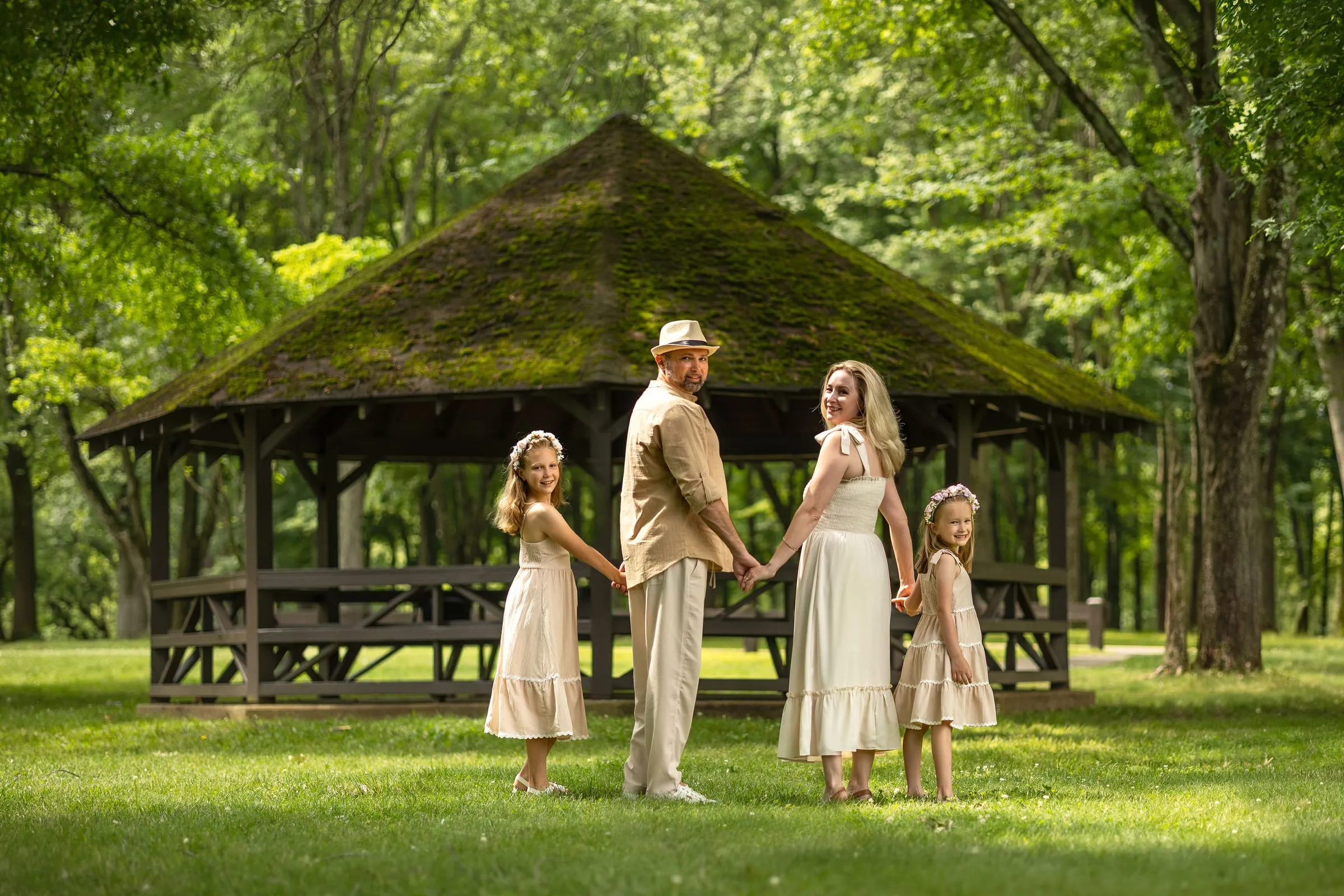 Family holding hands in front of a wooden gazebo with a mossy roof