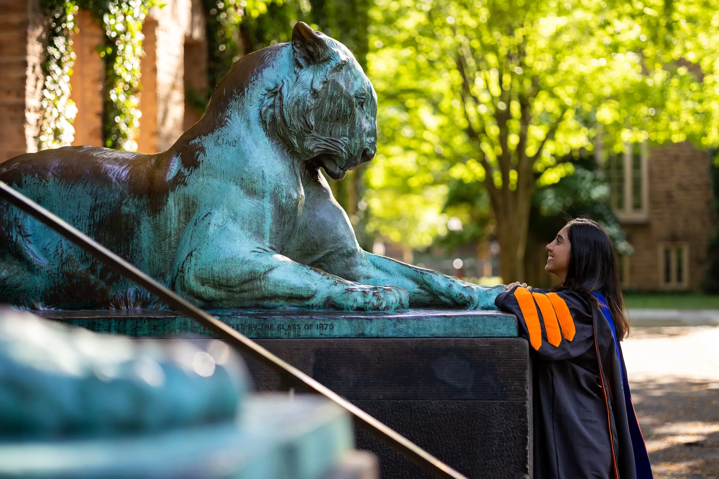 Graduate leaning on the pedestal of a bronze tiger, seen past the statue