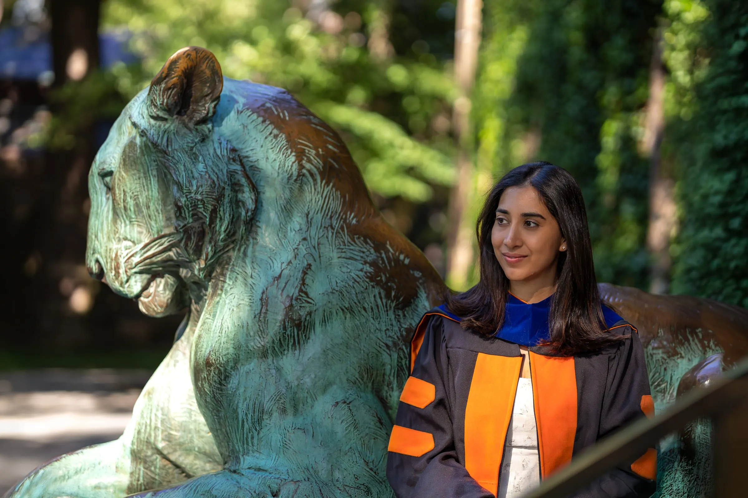 Graduate smiling beside a bronze tiger in the sunlight