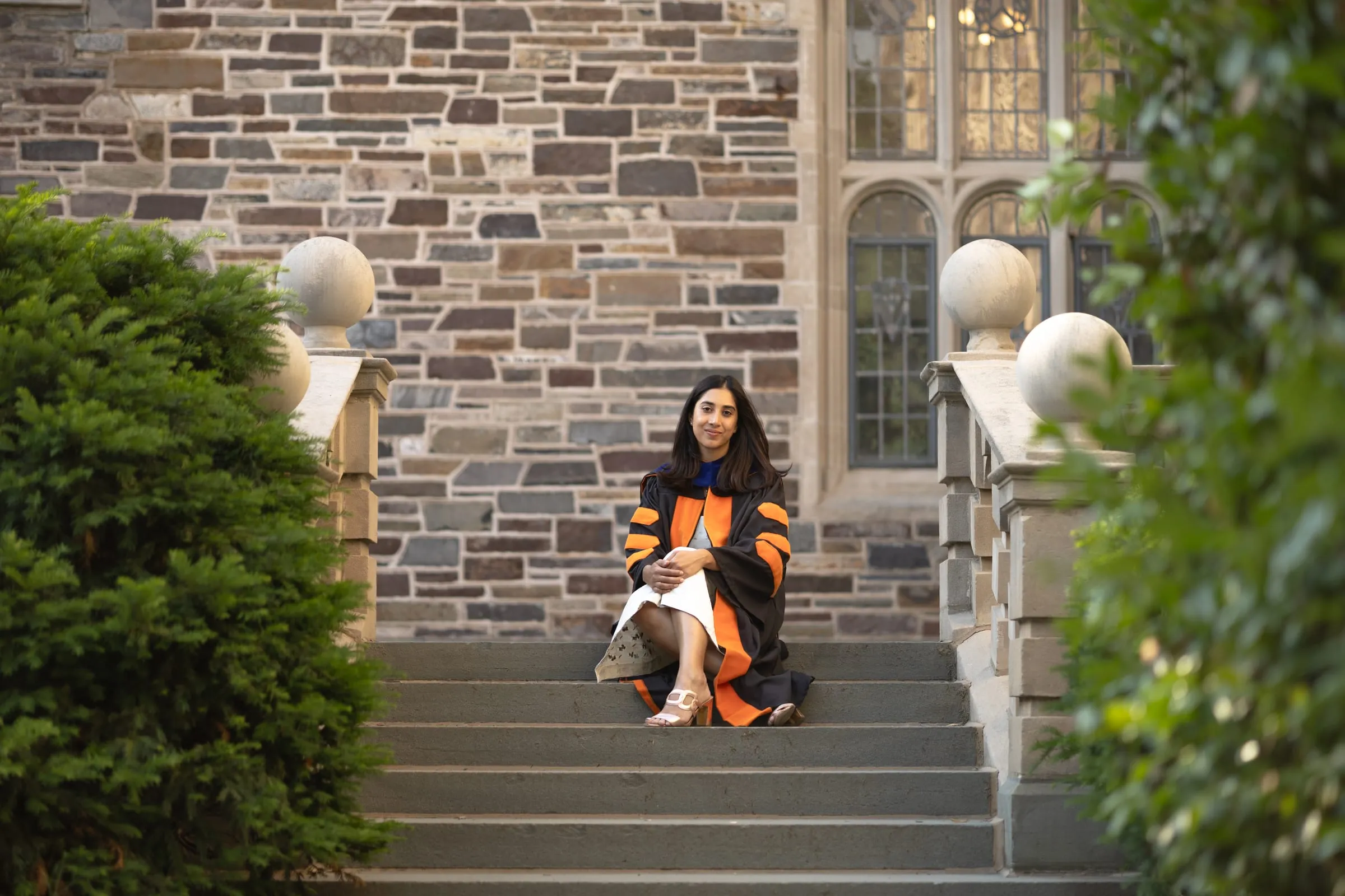 Graduate sitting on the stone steps of a Gothic building